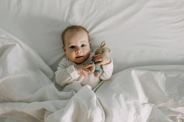 Μωρό Ξαπλωμένο Στο Κρεβάτι Καλυμμένο Λευκή Κουβέρτα Κρατώντας Ένα Παιχνίδι — Φωτογραφία Αρχείου