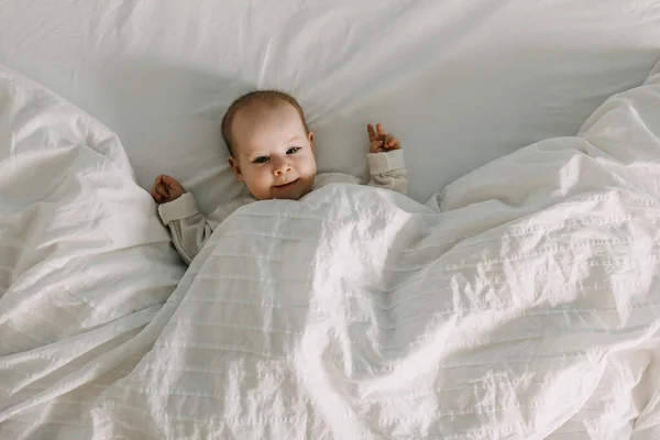 Bebé Feliz Acostado Cama Bajo Una Manta Blanca Suave Sonriendo —  Fotos de Stock