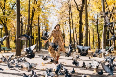 Genç bir kadın gülerek, sıcak bir sonbahar gününde Central Park 'ta güvercinlerin arasında koşuyor..
