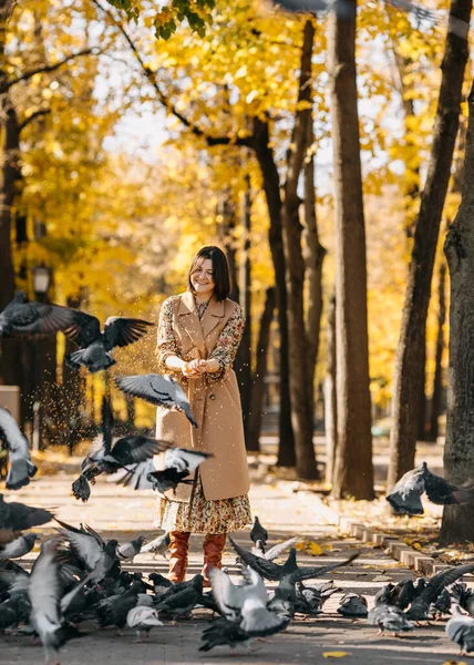 가을에 중심가 공원에서 여자가 미소짓고 비둘기에게 먹이를 — 스톡 사진