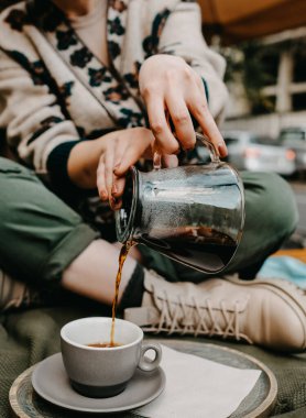 Açık havada, cam bir çaydanlıktan bardağa sade kahve döken birinin yakın çekimi..