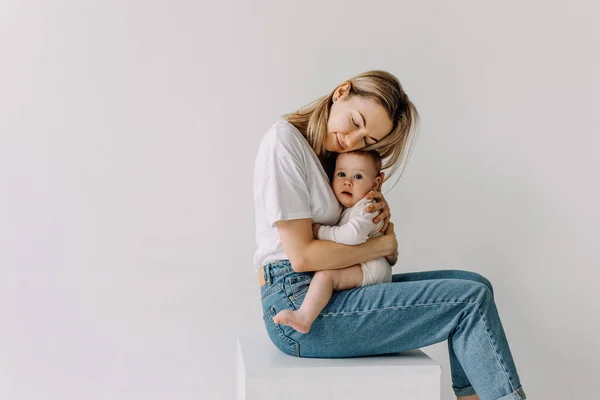 Mãe Sentada Abraçando Seu Bebê Fundo Parede Branca — Fotografia de Stock
