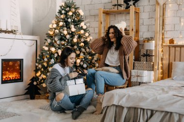Noel ağacı arka planında yerde oturmuş hediyeleri açan iki mutlu genç kadın..
