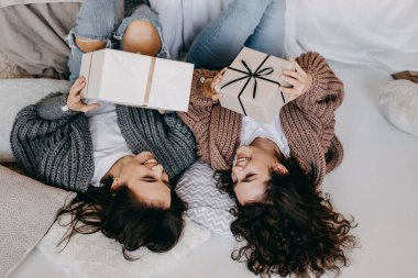 İki neşeli genç kadın yerde yatıyorlar, ellerinde hediye paketleriyle, gülümsüyorlar..