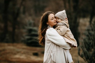Anne küçük kızını kucağında tutuyor, sarılıyor, dışarıda, bir parkta, sonbahar günü..
