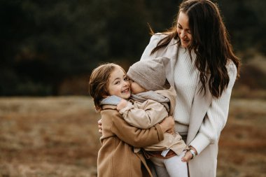 Anne sonbahar günü bir parkta çocuklarla vakit geçiriyor. Erkek kardeş kız kardeşi kucaklıyor..