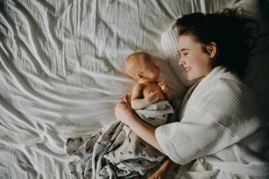 Anne ve yeni doğmuş bebek yatakta yatıyor, gülümsüyor, en tepede..