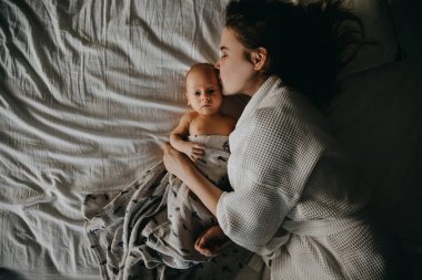 Anne ve yeni doğmuş bebek yatakta yatıyor. Anne öpücüğü bebek, üst manzara.