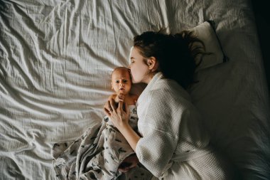 Anne ve yeni doğmuş bebek beyaz yatak çarşafında yatıyorlar. Anne öpücüğü bebek, üst manzara.