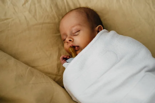 Newborn baby wrapped in a blanket, sleeping with a pacifier.