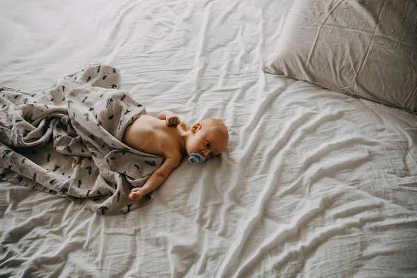 Miesięczne Dziecko Smoczkiem Pokryte Muślinowym Kocem Leżące Białym Prześcieradle — Zdjęcie stockowe