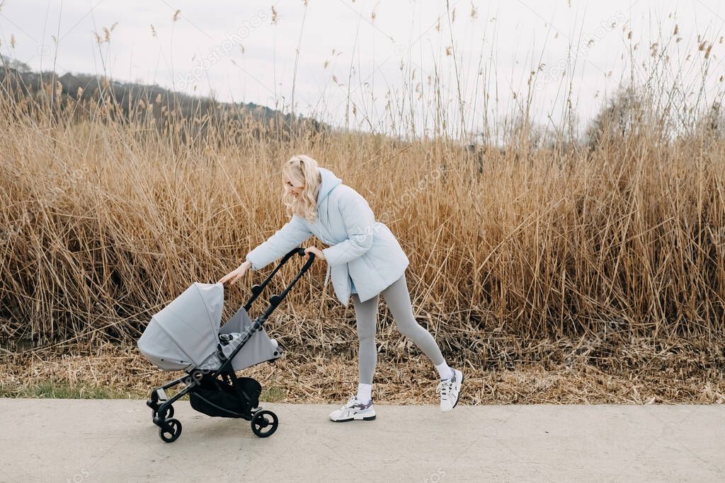 Blonde woman walking with a stroller by the lake in springtime. 