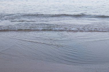 Güneş batmadan önceki sahilin manzarası, huzurlu ve sakin, deniz dalgaları ince kumu hafifçe vurur, rüzgarlı rüzgarla.