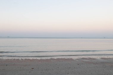 Güneş batmadan önceki sahilin manzarası, huzurlu ve sakin, deniz dalgaları ince kumu hafifçe vurur, rüzgarlı rüzgarla.