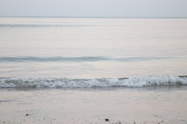 Güneş batmadan önceki sahilin manzarası, huzurlu ve sakin, deniz dalgaları ince kumu hafifçe vurur, rüzgarlı rüzgarla.