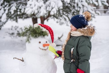 Mutlu sarışın şirin kız karlı kış yürüyüşünde bir kardan adama mektup verir.