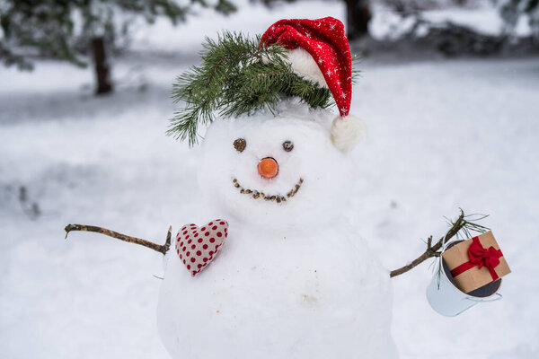 Snowman in santa hat outdoors. Funny snowman in a forest.