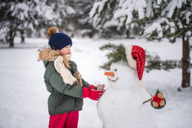 Mutlu, sarışın, tatlı kız bir kardan adamla oynaşıyor.