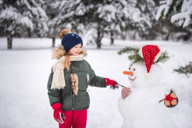 Mutlu, sarışın, tatlı kız bir kardan adamla oynaşıyor.