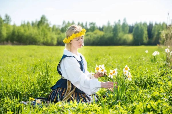 Mladá žena v národních šatech na poli s narcisy květiny. — Stock fotografie