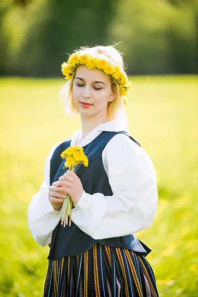 Jovem mulher em roupas nacionais vestindo coroa de dente de leão amarelo no campo de primavera. Primavera. — Fotografia de Stock