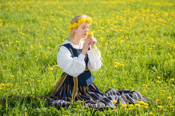 Mujer joven en ropa nacional con corona de diente de león amarillo en el campo de primavera. Primavera — Foto de Stock