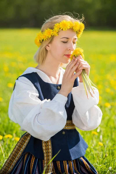 Junge Frau in Nationalkleidung mit gelbem Löwenzahnkranz auf dem Frühlingsfeld. Frühlingszeit — Stockfoto