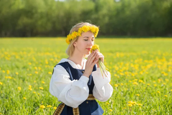 Jovem mulher em roupas nacionais vestindo coroa de dente de leão amarelo no campo de primavera. Primavera. — Fotografia de Stock
