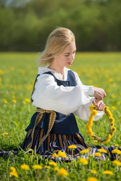 Junge Frau in Nationalkleidung mit gelbem Löwenzahnkranz auf dem Frühlingsfeld. Frühlingszeit — Stockfoto