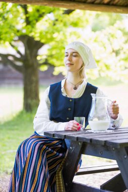 Doğada süt bardağı olan geleneksel giyinmiş bir kadın.