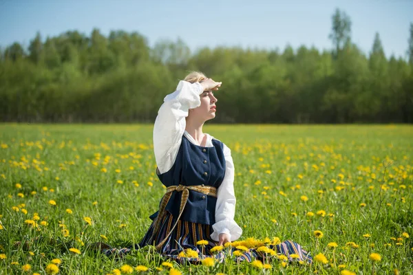 Jeune femme en vêtements nationaux portant une couronne de pissenlit jaune dans un champ de printemps. Printemps — Photo