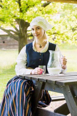 Doğada süt bardağı olan geleneksel giyinmiş bir kadın.