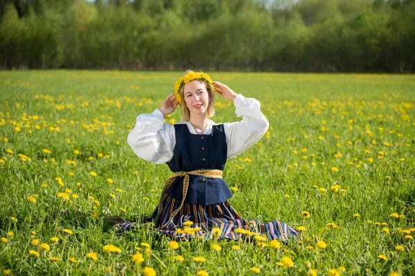 Νεαρή γυναίκα με εθνικά ρούχα που φορούσε κίτρινο στεφάνι πικραλίδας στο ανοιξιάτικο χωράφι. Άνοιξη — Φωτογραφία Αρχείου