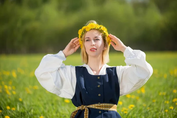 Jovem mulher em roupas nacionais vestindo coroa de dente de leão amarelo no campo de primavera. Ligo... — Fotografia de Stock