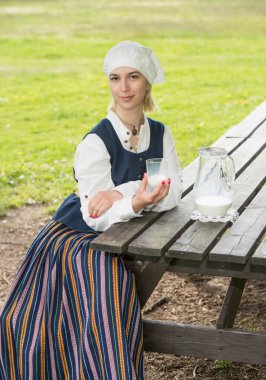 Doğada süt bardağı olan geleneksel giysili Letonyalı kadın.