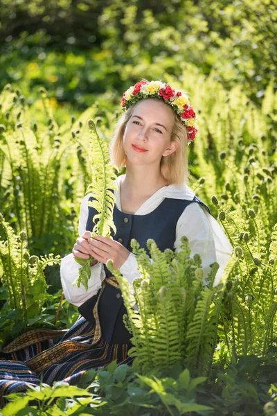 Jovem mulher em roupas nacionais e grinalda contra o fundo de uma samambaia verde. Ligo feriado letão — Fotografia de Stock