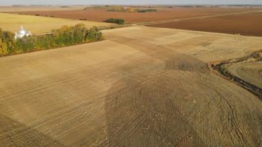 İnsansız hava aracı sonbahar renkleriyle hasat edilmiş tarlaların ve bir tarafı eski bir kilisenin üzerinde ilerliyor.