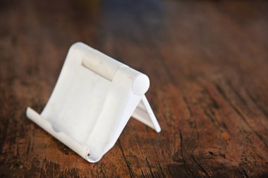 Plastik, beyaz renk, akıllı telefon tutacağı, kahverengi ahşap arka plana yerleştirilmiş.