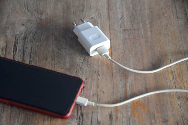 Bali, Endonezya - 08 Nisan 2022: Şarjlı akıllı telefon, kahverengi ahşap masaya yerleştirildi