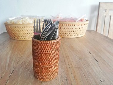 Kaşık ve çatallı Rattan camı, kahverengi ahşap masaya yerleştirilmiş.