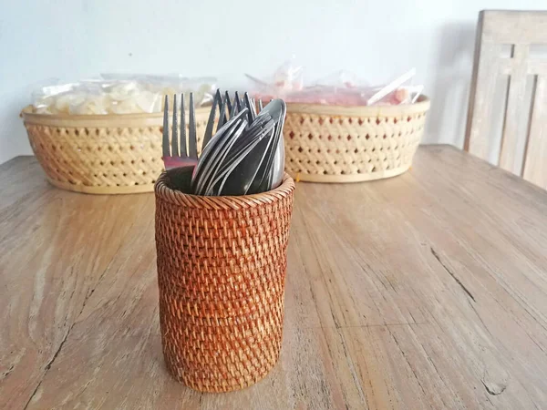 Kaşık ve çatallı Rattan camı, kahverengi ahşap masaya yerleştirilmiş.