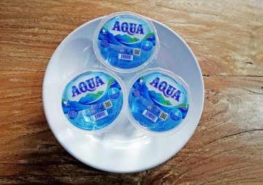 Bali, Endonezya - 16 Haziran 2022: Ünlü markalı üç bardak maden suyu, beyaz tabakta servis edildi ve kahverengi ahşap masaya yerleştirildi