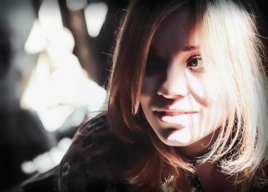 Pencereden süzülen parlak güneş ışığı genç ve çekici sarışın bir kadının gülümseyen yüzünü aydınlattı. Yüzeyin yüzeysel derinliği, zıt gölgeler, yumuşak seçici odak.