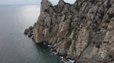 Karadeniz kıyısı, Kırım. 16 'nın 14' ünde kayaların üzerinden atlamak. Kayalık kıyılar, mavi sular, su yüzeyini kesen tekneler. Atış yeri Cape Kapchik, Sudak 'a yakın bir tatil köyü. 4K video, renk düzeltmesi yok.