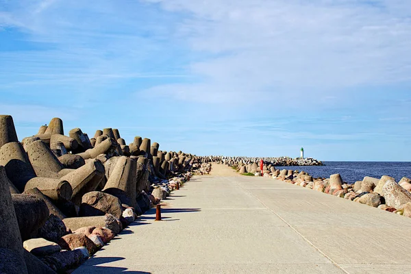 Road to a pier with a lighthouse, along the edges of the breakwater in Ventspils, Latvia.