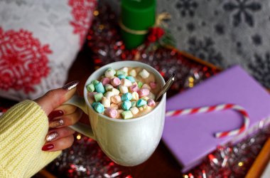 Sıcak bir akşam için, bir kadın kazağı içinde kakaolu bir kupayla ve lokumla yakın çekim. Bir kitap, bir mum, bir yastık, bir süs ve şeker kamışı ile ahşap bir tepsinin arka planında.