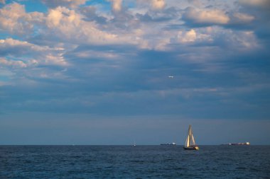Spain, Barcelona - May 29 2022: View of the Balearic Sea with small yachts and a beautiful sky with clouds before sunset.Against the background of cruise liner on the horizon and airplane in the sky.