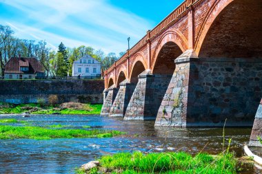 Kuldiga brick bridge across the Venta in Kuldiga, Latvia on a spring sunny day. Beautiful landscape with nature and architecture of the old town and the bridge.