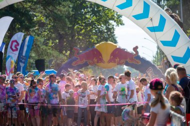 Jurmala, Kauguri, Latvia - August 14 2022: Close-up of the start of race on track with paints. Participants run in pink cloud of colored powder. Spectators behind the fence. The color run.