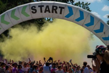 Jurmala, Kauguri, Latvia - August 14 2022: Close-up of the start of race on track with paints. Participants run in yellow cloud of colored powder. Spectators behind the fence. The color run.